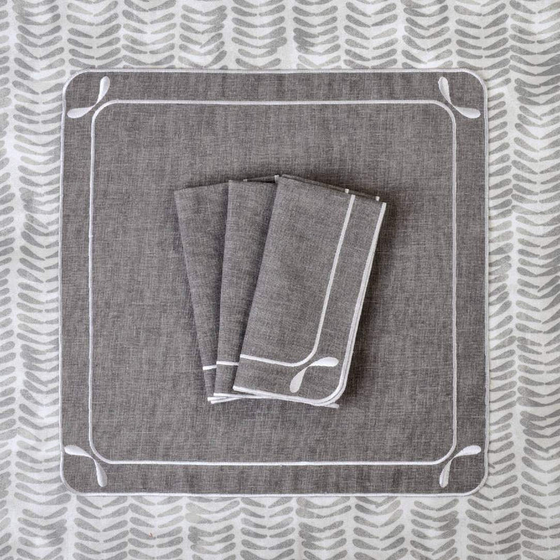 Folded Dragonfly embroidered cotton napkins in grey on tablecloth from the same collection.