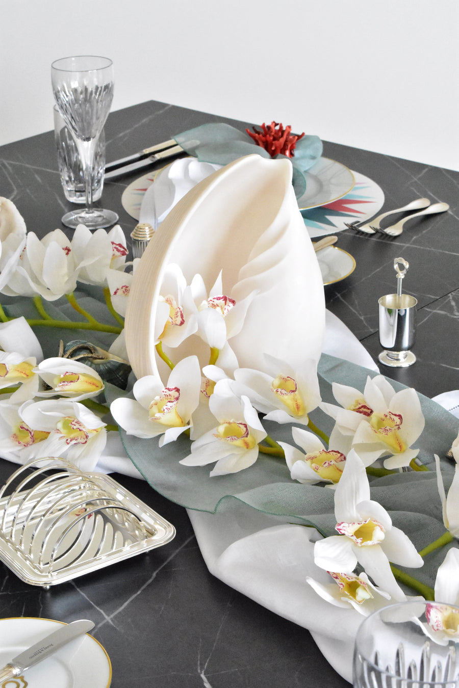 Elegant table setting with white orchids, silverware, and decorative elements on a dark surface.