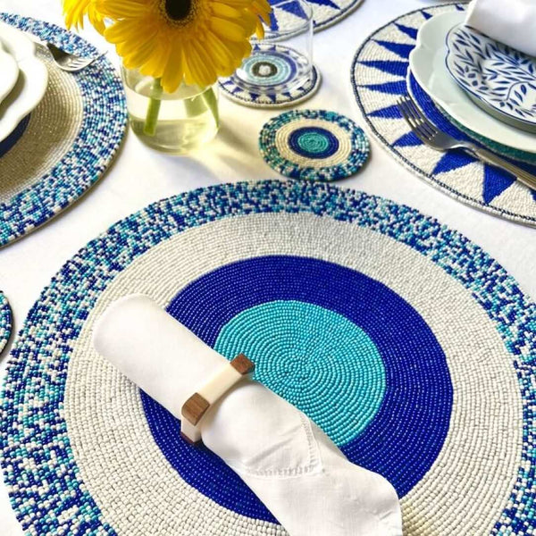 Blue hand-beaded placemat with geometric circle pattern on mediteranean table setting.