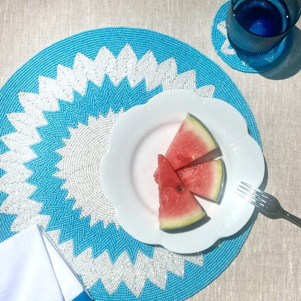 Blue and white hand-beaded placemat in Mediterranean style on outdoor summer table.