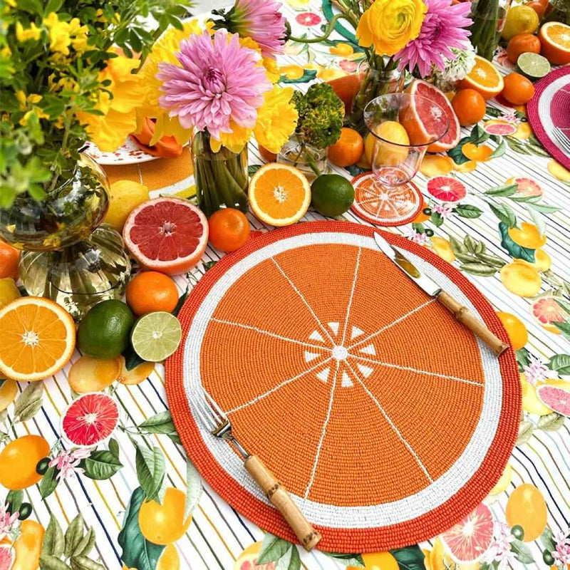 Orange hand-beaded placemat by Von Gern Home on summer table side view.