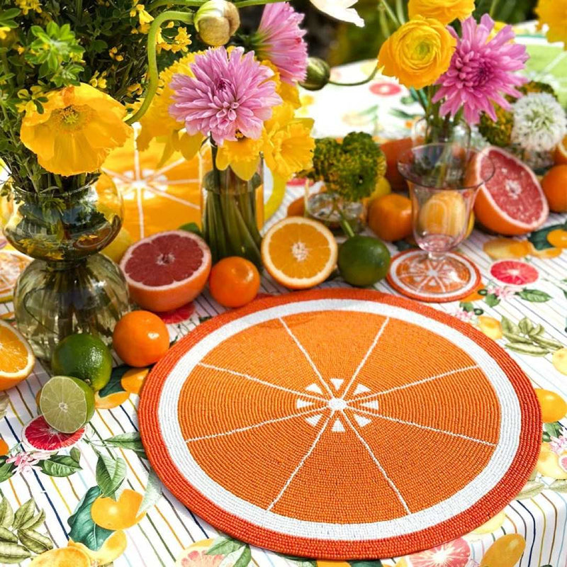 Orange hand-beaded placemat by Von Gern Home next to floral citrus centrepiece.