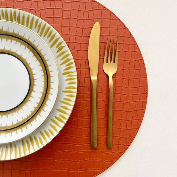 Croco reversible placemat in orange and moss green faux leather showing orange side, close-up.
