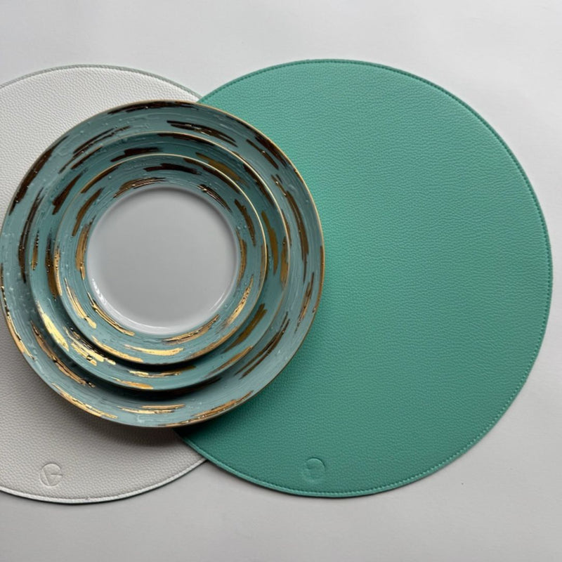 Reversible placemat in turquoise and white faux leather styled on modern tablescape.