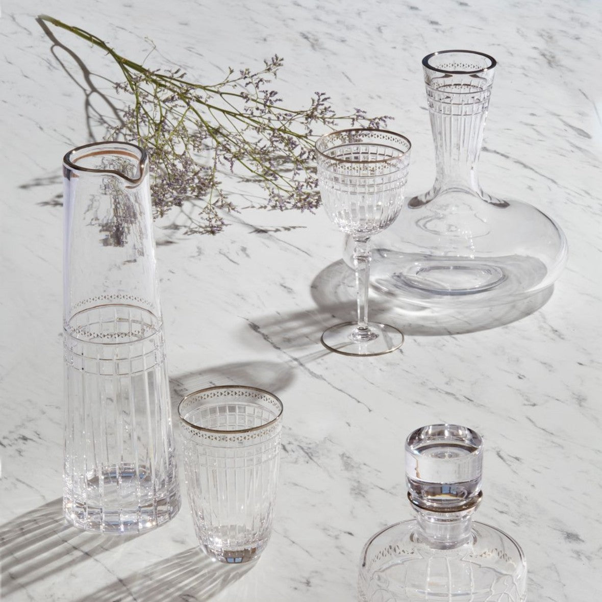 Set of Aghata Platinum crystal glass with geometric cuts by Cristallerie de Montbronn on a marble surface with decorative elements.