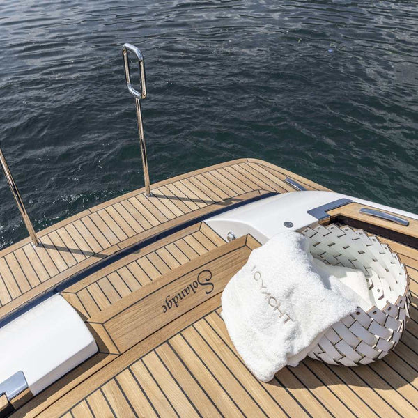 Wooden deck of a yacht with a Almeria small round storage basket in cream regenerated leather by Pinetti, hand-woven and suitable for outdoor use