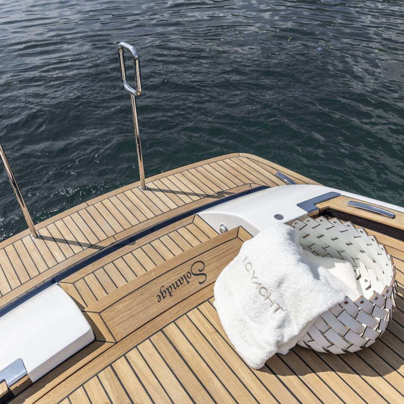 Wooden deck of a yacht with a Almeria small round storage basket in cream regenerated leather by Pinetti, hand-woven and suitable for outdoor use