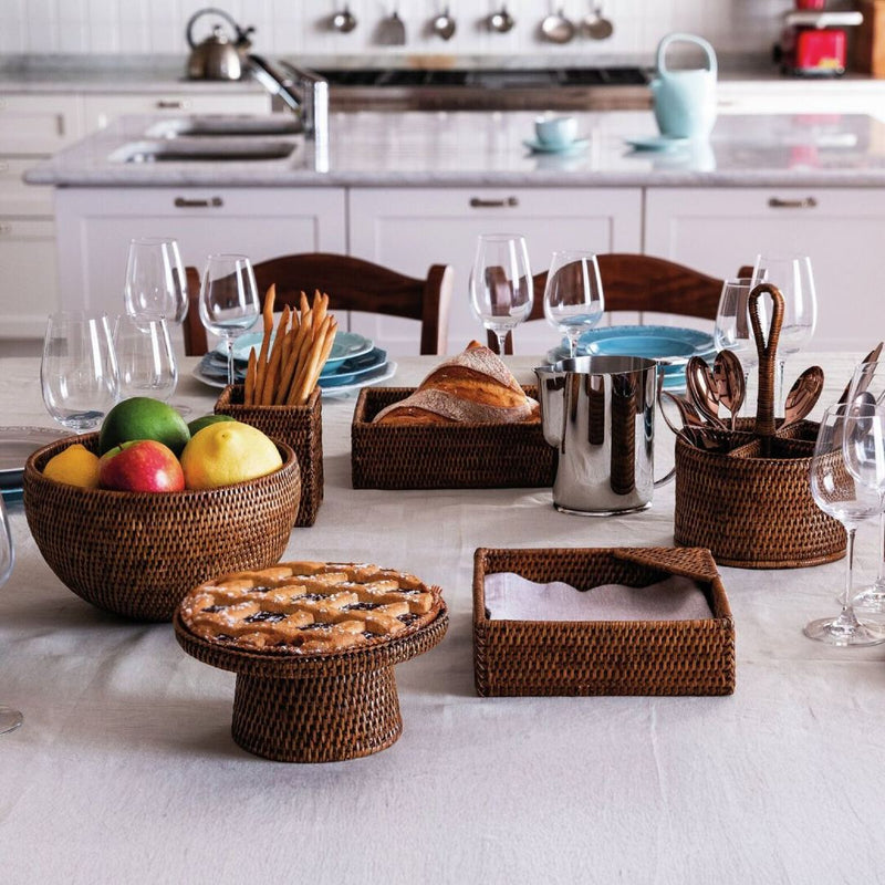 Handwoven brown rattan cutlery and condiment holder next to other rattan serving accessories.