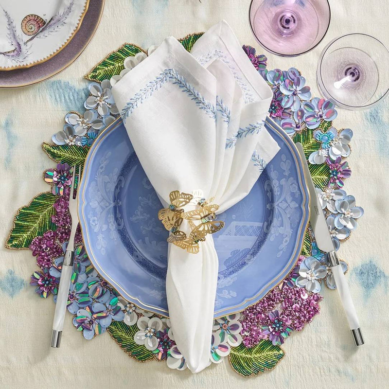Top view of Kim Seybert Jardin napkin with periwinkle embroidery, styled with floral placemat, Amiramour