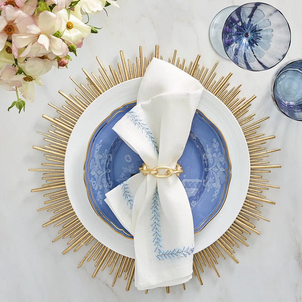 Top view of Kim Seybert Jardin napkin with periwinkle embroidery, styled with gold place charger, Amiramour