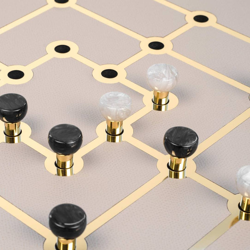 Close-up of Mill Game Set in Cream Grained Leather with gold detailing and eco-shell pawns by Pinetti on a geometric patterned surface.