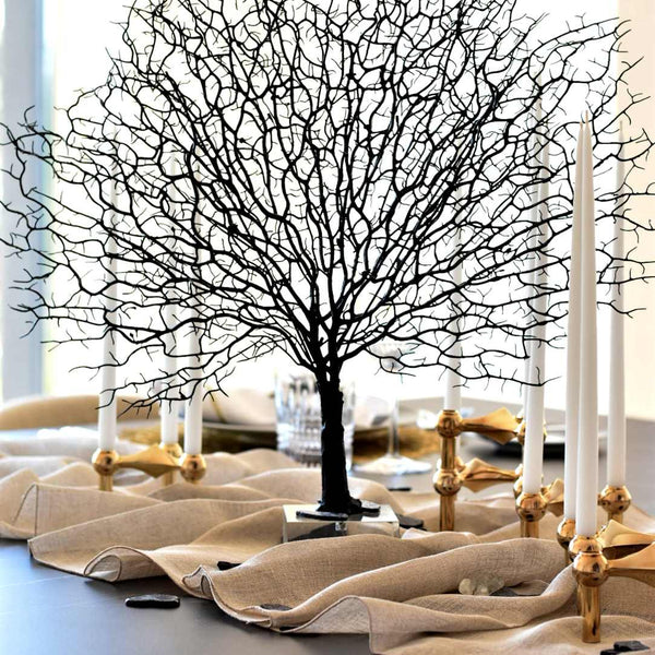 artificial fan tree in black with a glass stand decorated on a table with a beige runner and gold candles