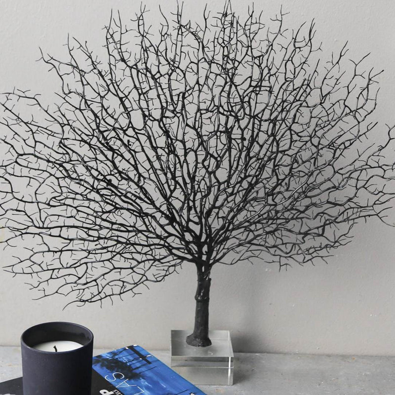Black artificial tree on a gray surface with a candle and book in the foreground