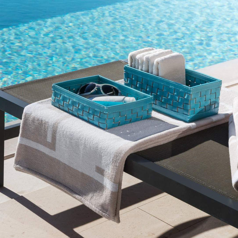 Two blue Barcellona rectangular low basket in turquoise outdoor leather by Giobagnara x Riviere, handwoven design suitable for indoor and outdoor use on a lounge chair by a pool