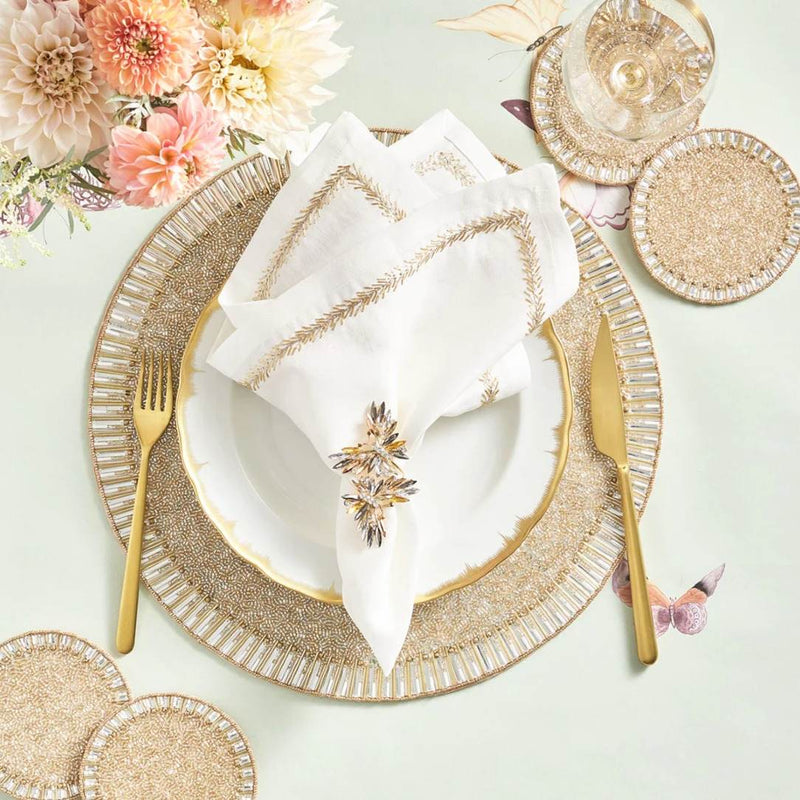 Elegant table setting with gold plates, cutlery, and floral decorations on a light background