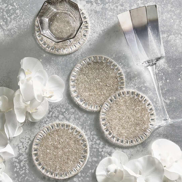Silver coasters on a textured surface with white flowers and a glass.