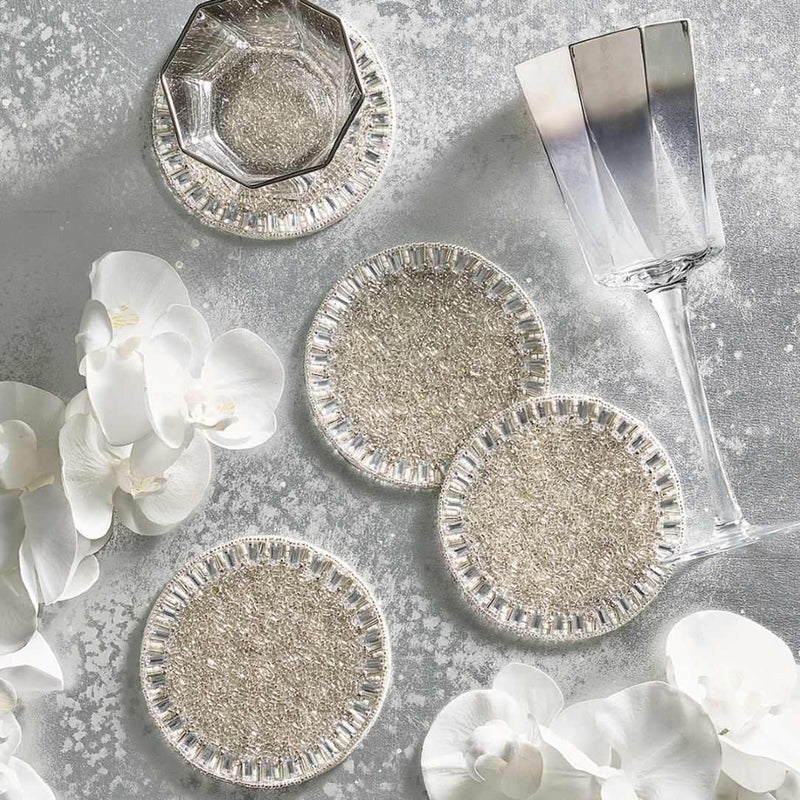 Silver coasters on a textured surface with white flowers and a glass.
