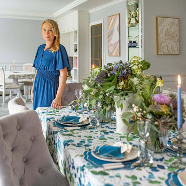 Woman in a blue dress standing by a decorated dining table with floral arrangements.