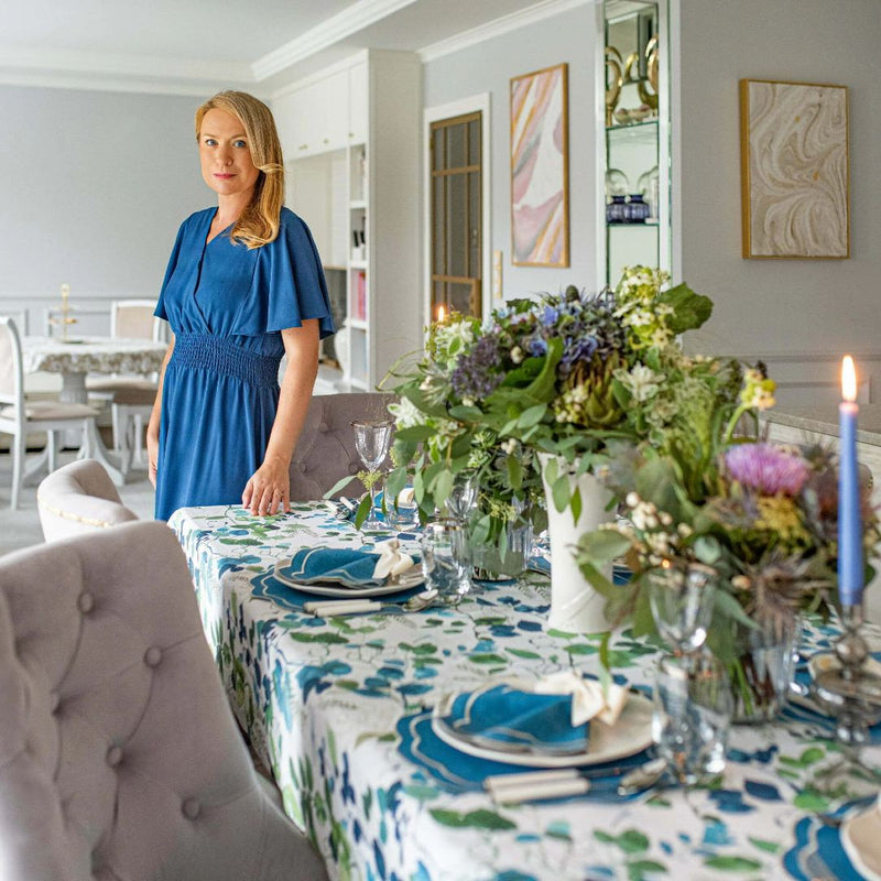Woman in a blue dress standing by a decorated dining table with floral arrangements.