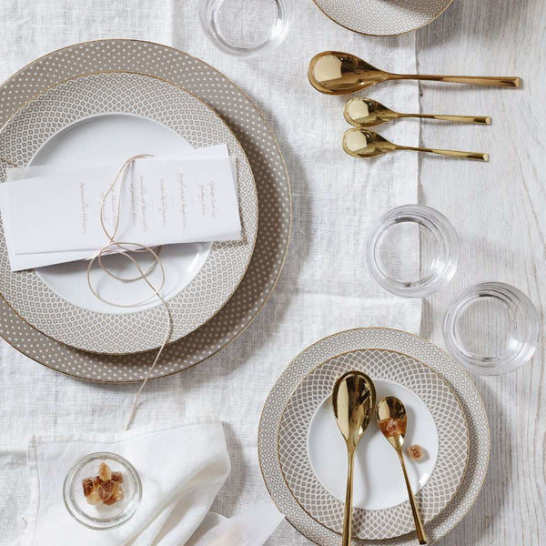 Elegant table setting with Francis Carreau Beige porcelain bread and butter plate with beige and gold check design by Rosenthal, gold cutlery, and clear glasses on a white tablecloth.