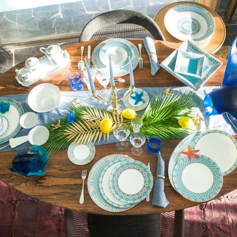 Dining table set with Portofino decorative plates, glasses, and a centerpiece on a wooden table.