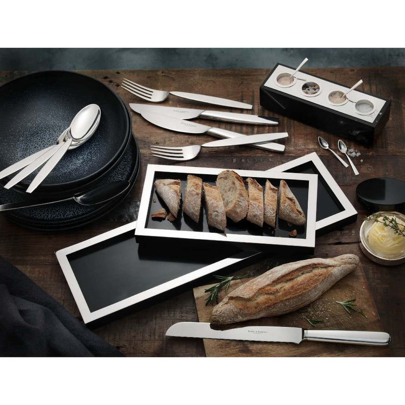 Table setting with black plates, silver cutlery, and silver-plated bread tray with black base by Robbe & Berking on a wooden surface.