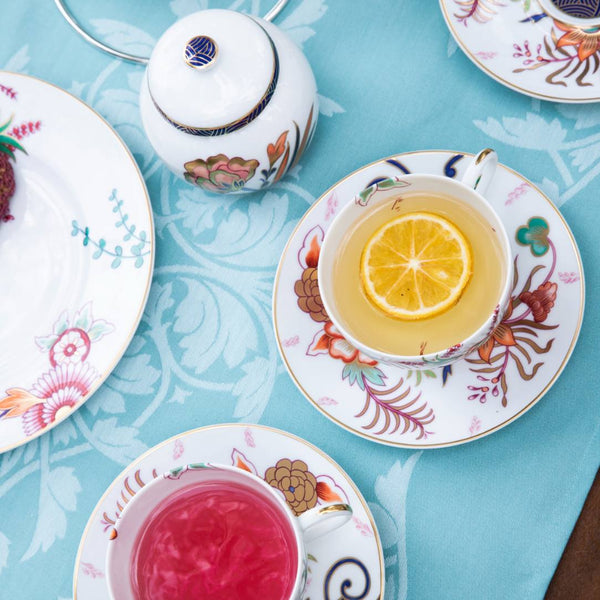 Tea cups with lemon and pink tea on decorative saucers on a blue tablecloth.