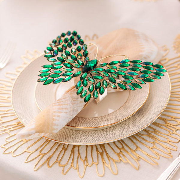 Decorative green butterfly on a plate with gold rim and shell, placed on a textured surface.