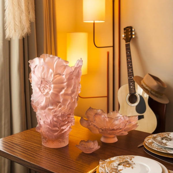 Pink glass vase and bowl on a wooden table with a guitar and hat in the background.