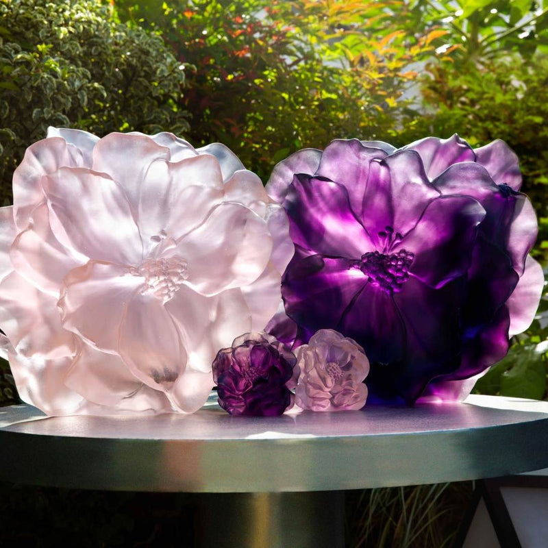 Two large glass flower sculptures, one pink and one purple, on a table with a natural background.