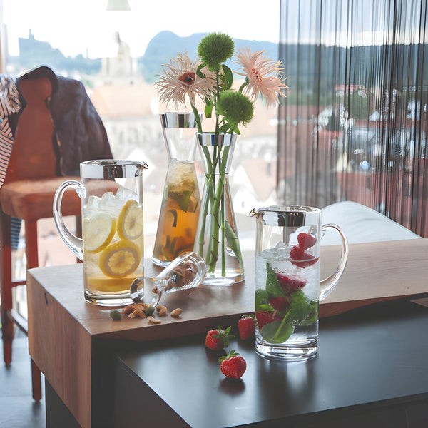 Table with glasses of iced tea and water, a vase with flowers, and strawberries on a wooden surface.