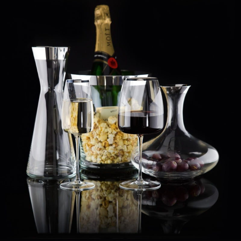 Two wine glasses with red and white wine, a bottle of champagne, popcorn, and grapes on a black background.
