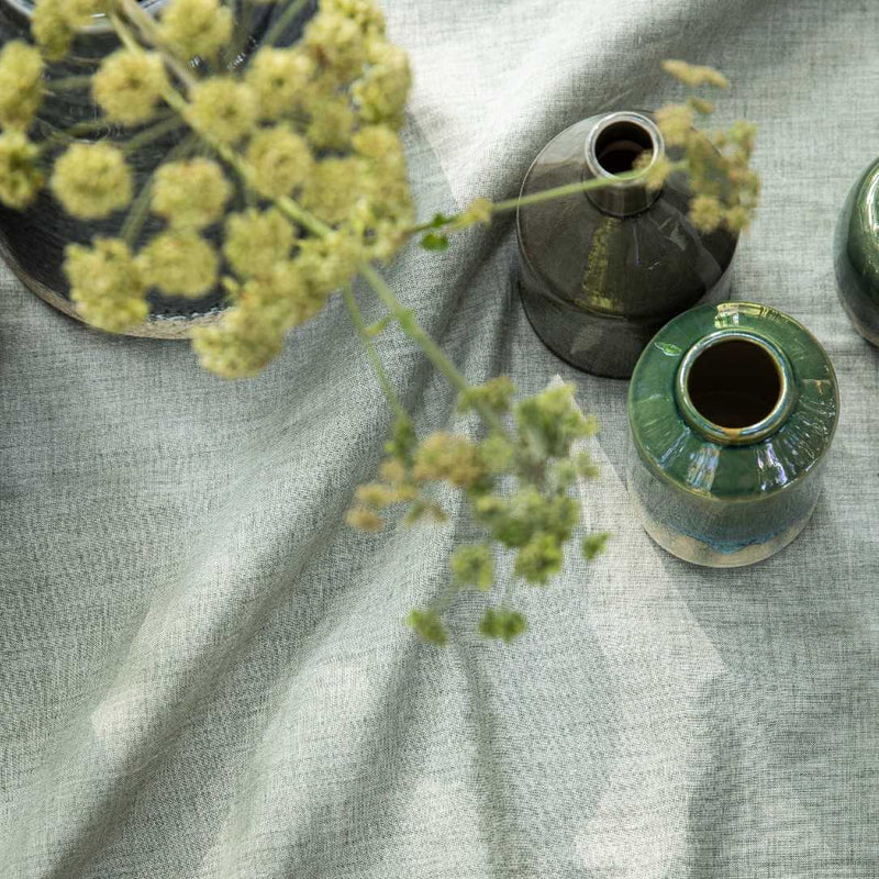 Green ceramic vase with floral arrangement on a textured fabric surface