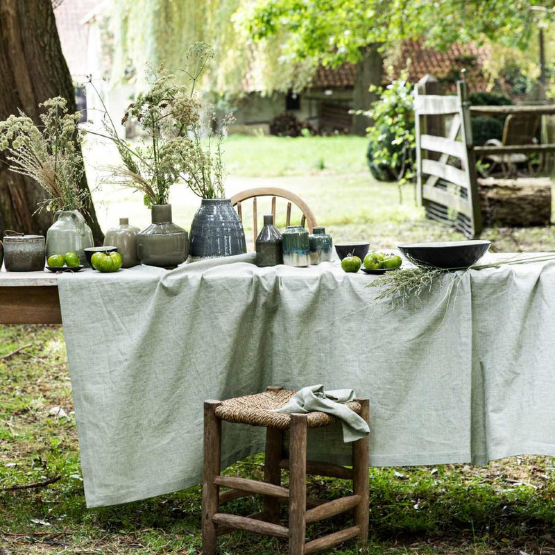 Outdoor setting with a table covered in a green cloth, surrounded by nature.