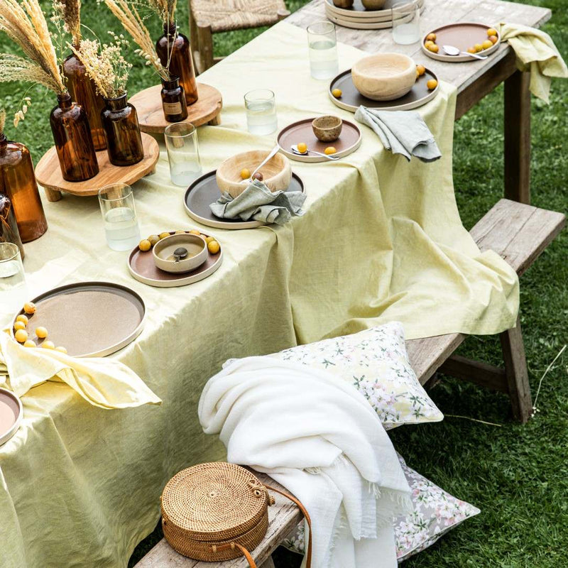 Outdoor table setting with a yellow tablecloth, decorative items, and glasses on a grassy background.