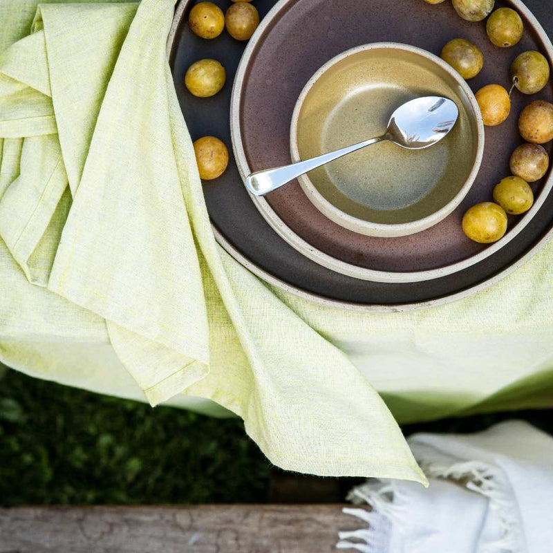 Close-up of a bowl with soup and a spoon, surrounded by lemons and a green napkin.