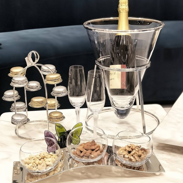 Champagne bottle in a Glass and silver-plated champagne bucket Éclat by Ercuis on a modern stand with glasses, nuts, and a butterfly decoration on a table.