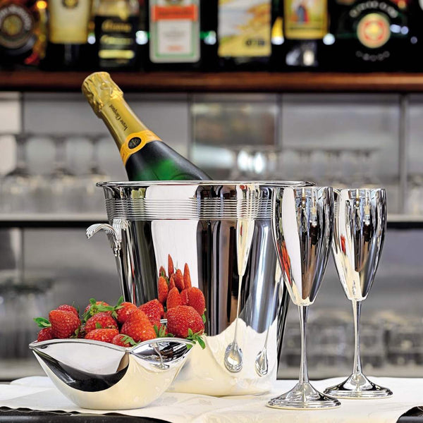 Champagne bottle in a Silver-plated champagne bucket with ribbed detailing and handles by Greggio, two silver champagne flutes, and a silver bowl on a bar counter.