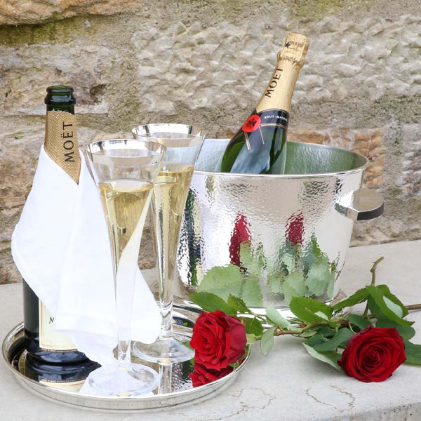 Champagne bottles, glasses, and ice bucket with red roses on a stone surface