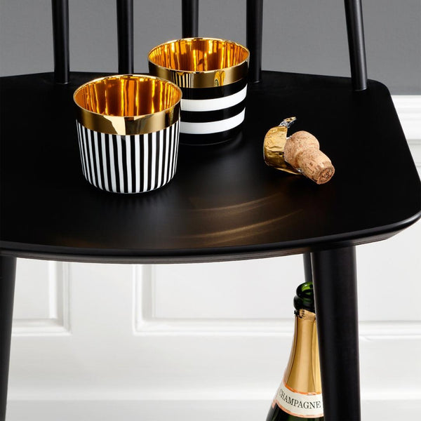 Two gold and black striped cups on a black table with a bottle of champagne and cork.