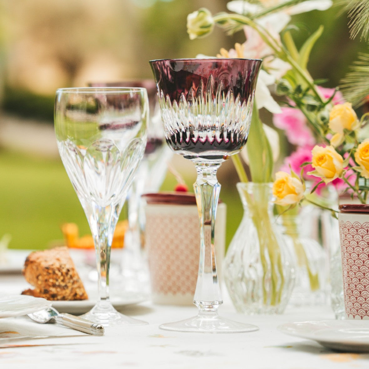 Chartres crystal glassware with bold bevel cuts inspired by Gothic architecture, by Cristallerie de Montbronn on a table with flowers and food in the background