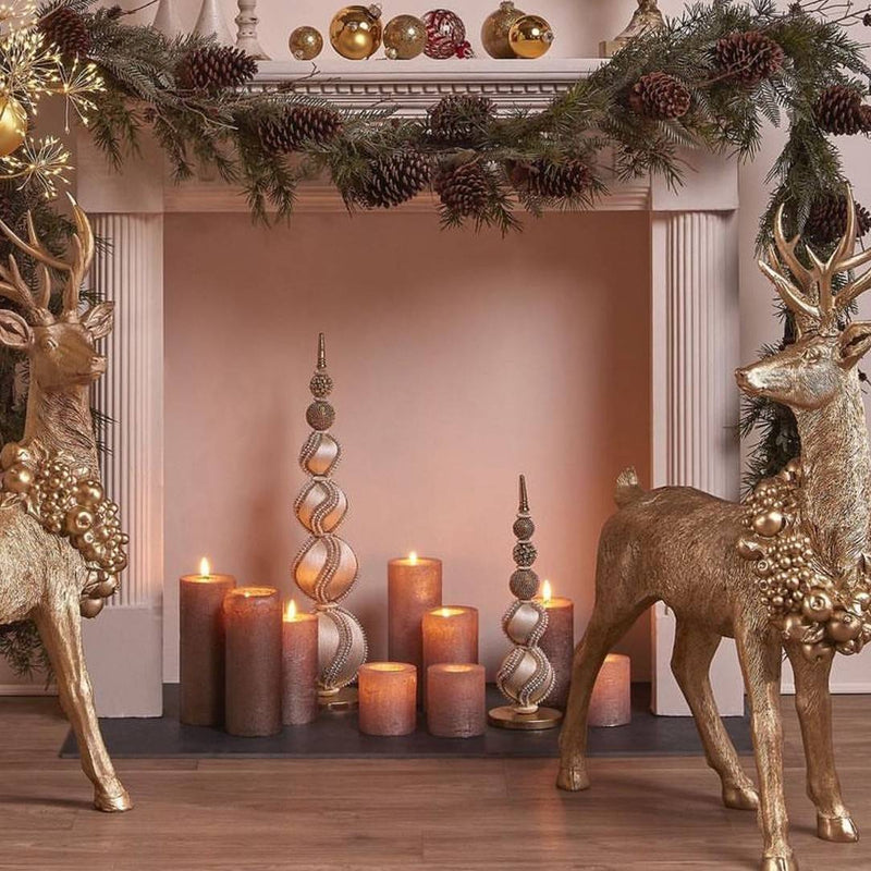 Decorative Christmas scene with gold reindeer, candles, and a garland on a fireplace.
