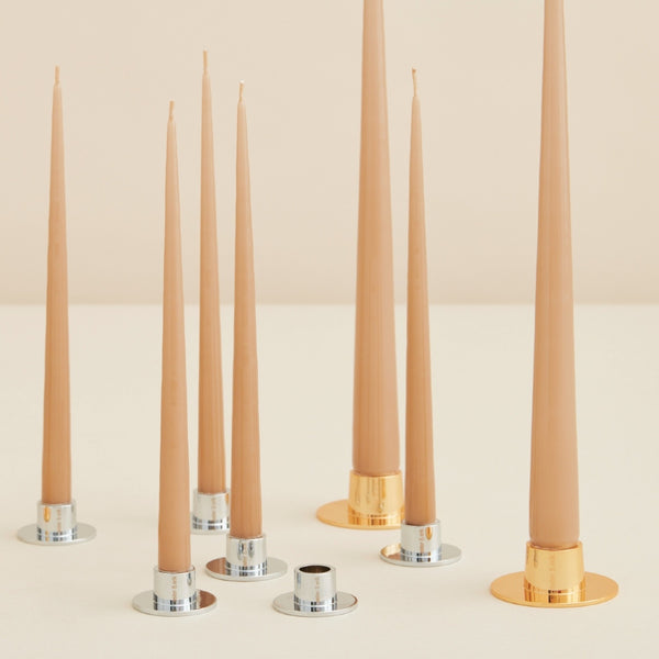 Set of tall, thin candles with metallic candle holders on a light background