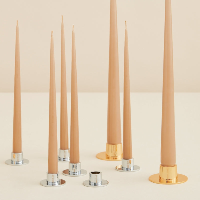 Set of tall, thin candles with metallic candle holders on a light background