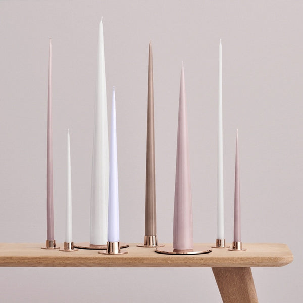 Set of tall, thin candles on a wooden stand against a light gray background