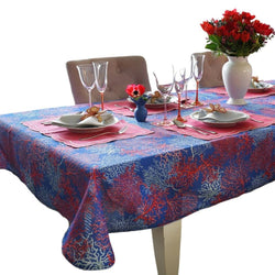 Dining table set with a blue and red patterned tablecloth, plates, glasses, and flowers.