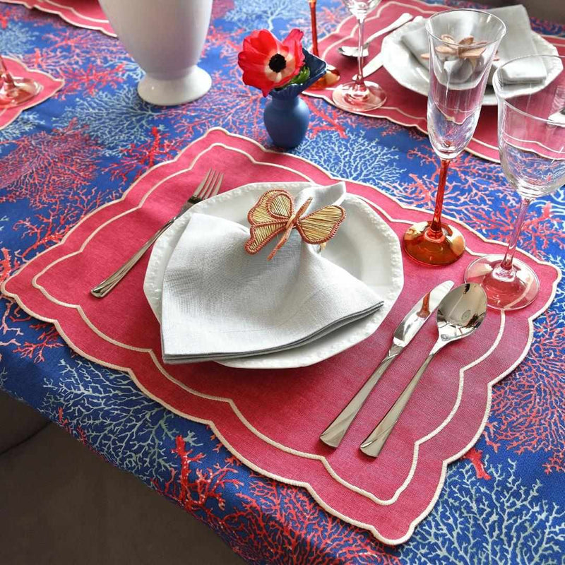 Table setting with red and blue tablecloth, pink placemat, and white plates.