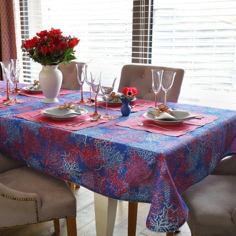 Dining table set with a blue and red patterned tablecloth, pink placemats, and floral centerpieces.