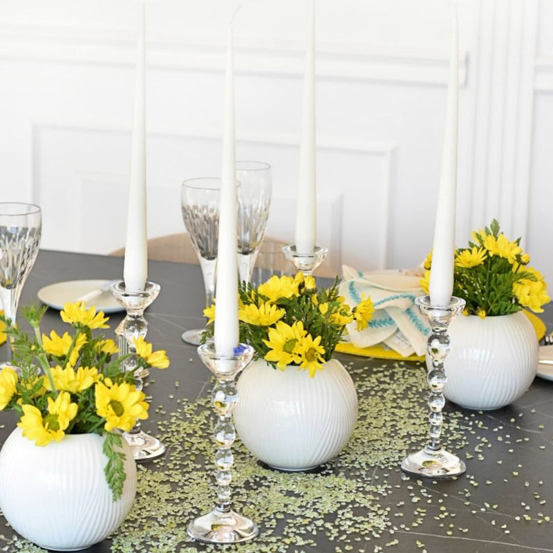 Decorative table setting with yellow flowers, white candles, and crystal candle holders on a gray tablecloth.