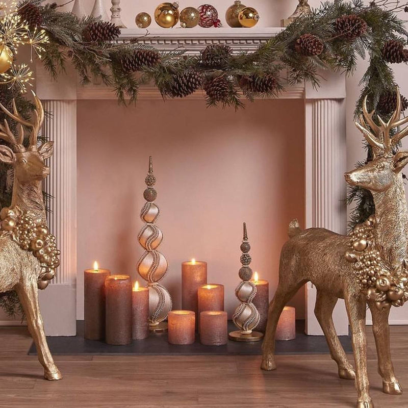 Decorative setup with gold deer, candles, and a garland on a fireplace.